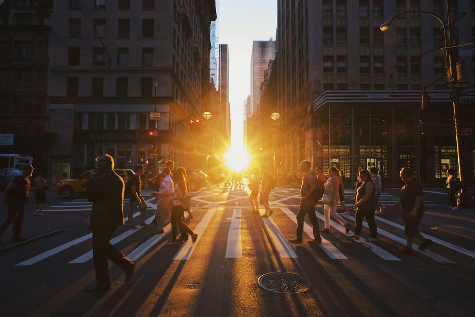 People cross a road as a sunset shines through buildings in the background. Salesforce is sunsetting startup Clockwise